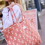 Detailopname van een olijfgroene gewatteerde shopper met een verfijnde blokprint, gedragen door een model op een buitenevenement.