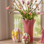 Combinatie van een groot (15 cm) en klein (11 cm) gestreept keramisch paasei in een sfeervolle setting met een roze vaas .