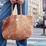 Close-up van een ruime okergele katoenen shopper met handbedrukte bloemenmotieven, gedragen aan de hand