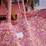 Close-up van het witte merklabel Bonheur du Jour Paris op een roze gewatteerde stof met bloemen.