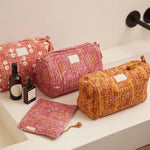 Assortiment handgemaakte gewatteerde toilettassen van Bonheur du Jour Paris in terracotta, roze en okergeel met bloemenprints in een badkamer setting.
