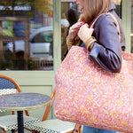 Detail van de schouderbanden en het stikwerk van een roze gewatteerde tas met botanische print.