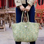 Een vrouw draagt een grote, olijfgroene quilted shopper van katoen met een verfijnde bloemenprint over haar schouder in een stedelijke omgeving.