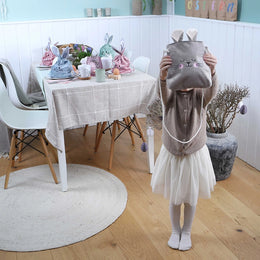 Een kind draagt een bruin fluwelen paastasje met lange konijnenoren en roze binnenkant op de rug tijdens het buiten spelen in de lente