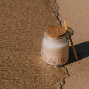AZUR Sunset Dreams magnesium badkristallen in het natte zand terwijl een zachte golf over de bodem van de pot spoelt.
