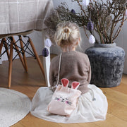 Sfeerbeeld van een kind met een roze velvet schoudertasje met konijnenoren tijdens het versieren van de paastak