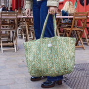 Close-up van een ruime groene katoenen shopper met handbedrukte bloemenmotieven, gedragen aan de hand