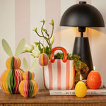 Twee meerkleurige honeycomb paashazen in verschillende groottes staan ter decoratie op een houten dressoir naast een gestreepte vaas en paasaccessoires.