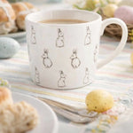 Gedekte tafel met porseleinen mok met konijntjes en paaslekkernijen in lente interieur