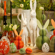 Sfeervolle paastafel met verschillende witte en groene paasaccenten, keramische vazen en papieren paasversiering.