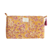 Close-up van een okergele quilted katoenen toilettas met een verfijnde witte bloemenprint en een wit kwastje aan de rits.