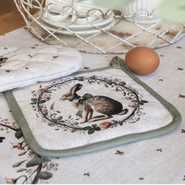Landelijke beige pannenlap met groene bies en een print van een konijn in een krans, liggend op een bijpassend tafelkleed.