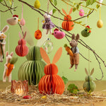 Creatieve lente decoratie met een peach honeycomb haas en andere hangende paasaccenten aan voorjaarstakken.