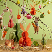 Creatieve lente decoratie met een peach honeycomb haas en andere hangende paasaccenten aan voorjaarstakken.